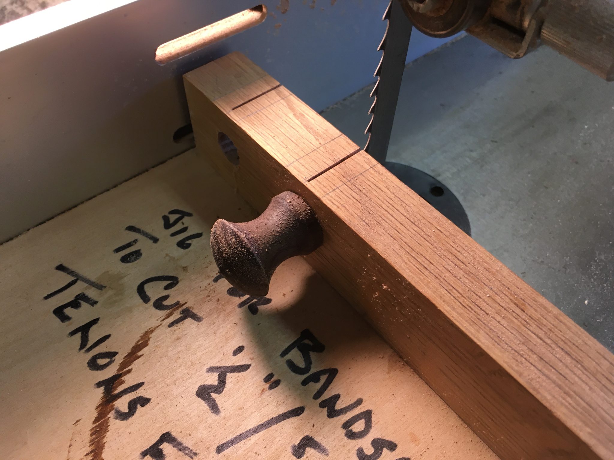 This jig makes it easy to cut a kerf into the exact center of the tenon on a turned knob.  Simply drill a hole (or as many holes as you have sizes of tenons) in a piece of scrap wood sized so the tenon fits snugly.  Mount it to the edge of a square piece of plywood.  Insert the knob, make the cut