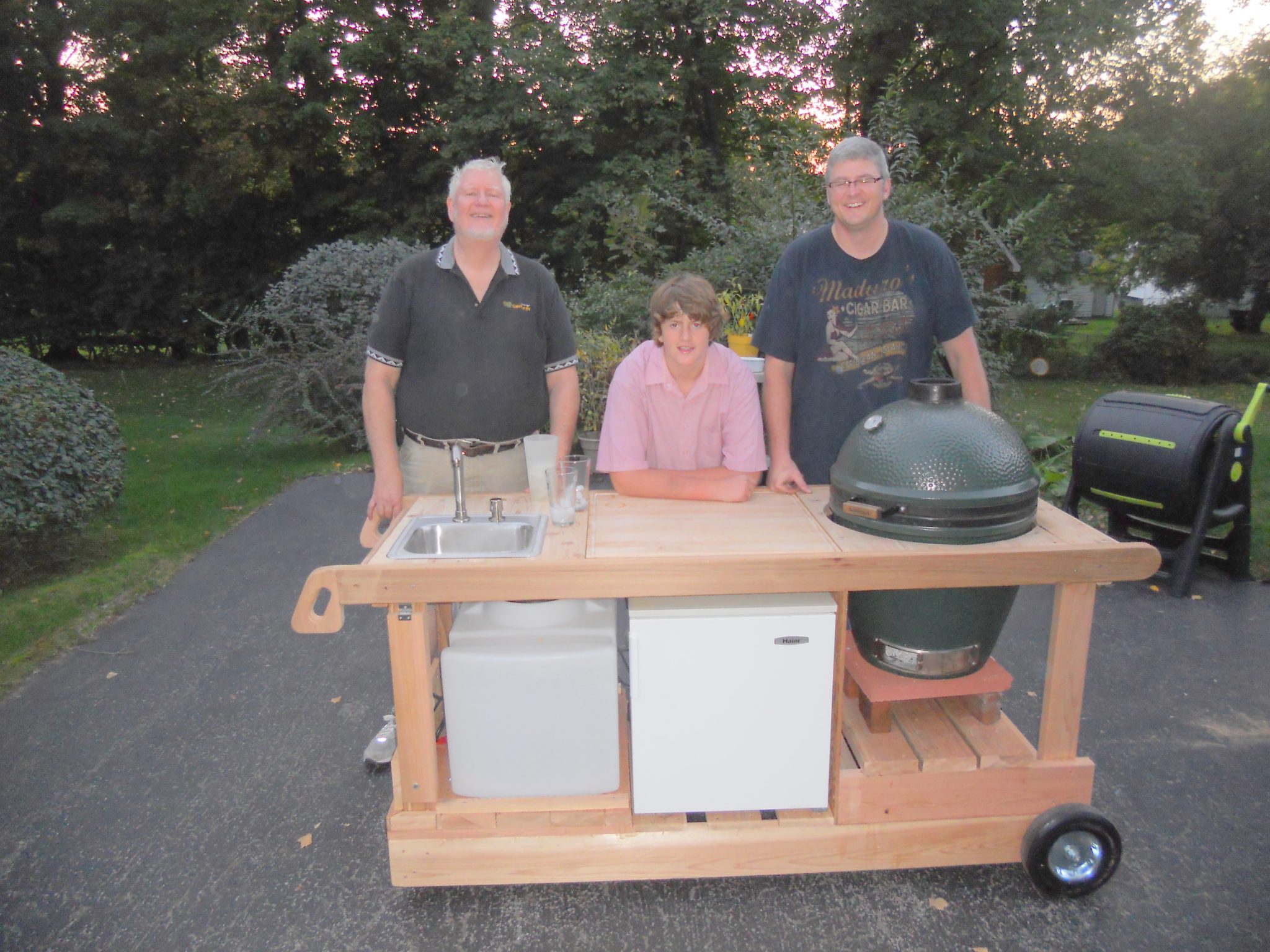 BBQ Cart with sink, Water tank, Refrig, Big Green Egg Cooker, & cutting board.  Built for My Middle son. Shown with Grandson.  Made from Cedar.